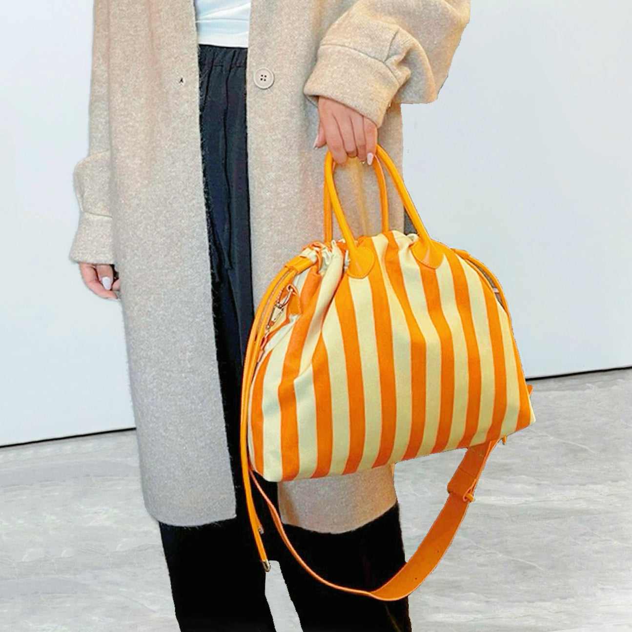Close-up of model holding orange striped bag by the grab handle; highlighting the drawstring closure and PU leather detail.