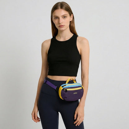 A model wearing the deep purple AOIO belt bag around the waist over dark leggings.