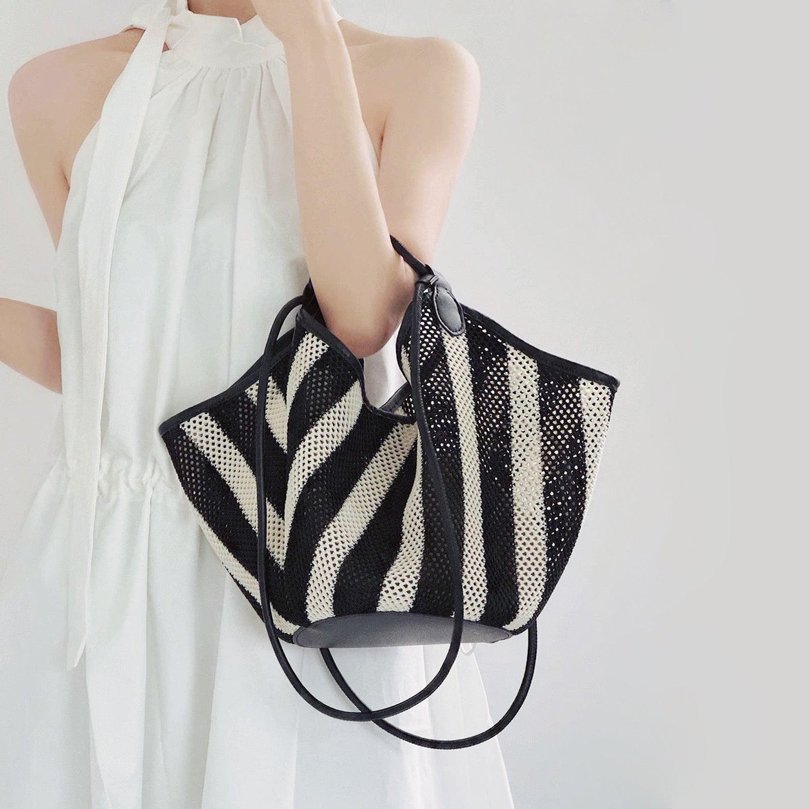 Model carrying a Black and white striped basket bag handheld, great for daily carry and travel.