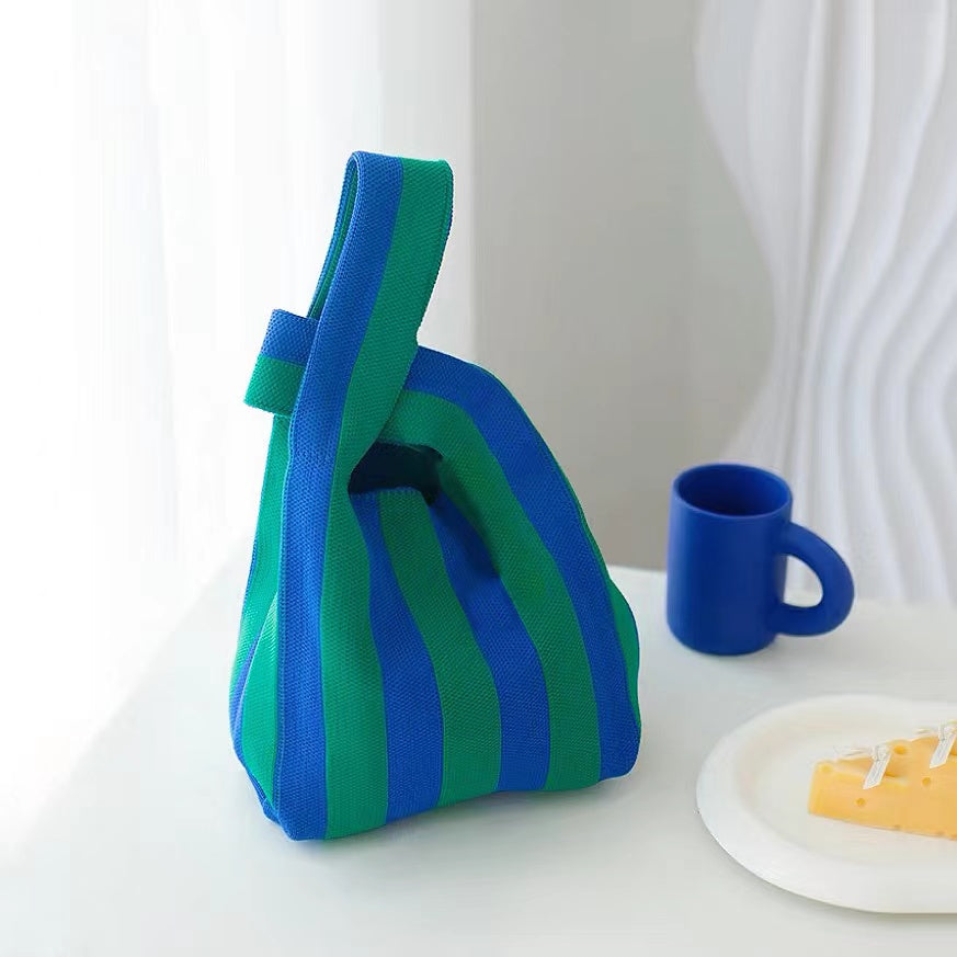 A blue and green vertical stripe knit tote bag placed on a table with a blue mug, perfect for aesthetic lifestyle photography.
