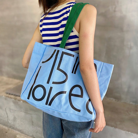 Model wearing a blue Bold Letter Canvas Tote Bag, trendy bold graphic bag for Urban Creatives and daily utility.