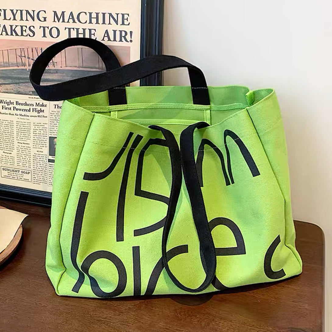 Front view of the green canvas tote bag with black graphic letters.
