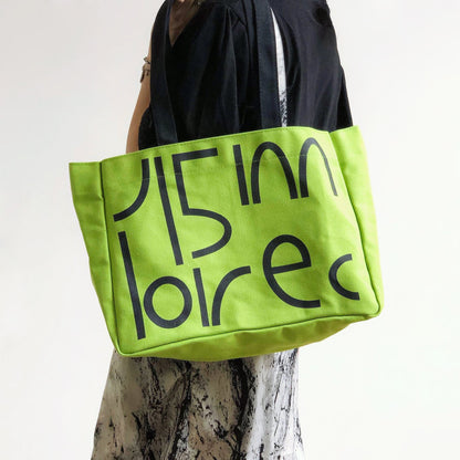 Side view of a model styling the  green bold letter tote bag; vibrant aesthetic fashion accessory.