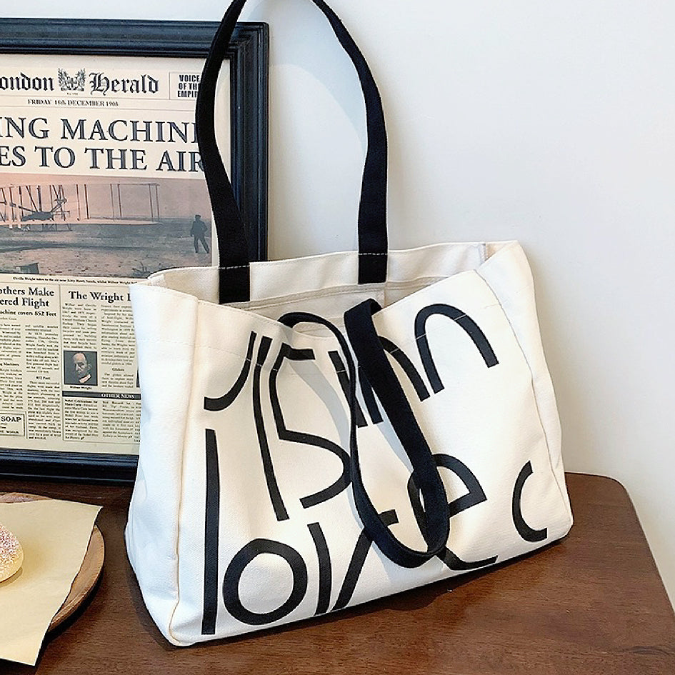 Front view of White canvas tote bag with bold black letter print.