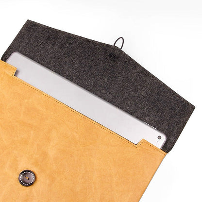 Caramel Tyvek laptop sleeve with a dark felt interior, button and cord closure, holding a silver laptop.