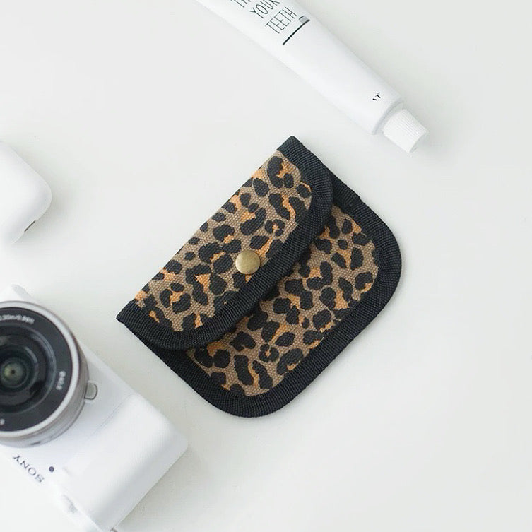Leopard print canvas coin purse with black trim; snap-flap pouch for coins, lip balm, and small items.