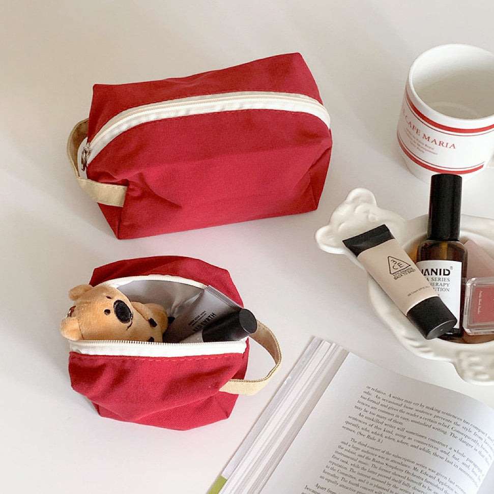 Open red canvas pouch with a small teddy bear and cosmetics; portable travel organizer for personalized items.