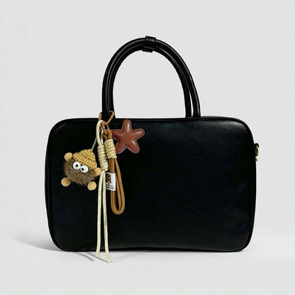 Brown coalball star charm attached to a minimalist black leather tote bag; stylish bag personalization for daily commute.