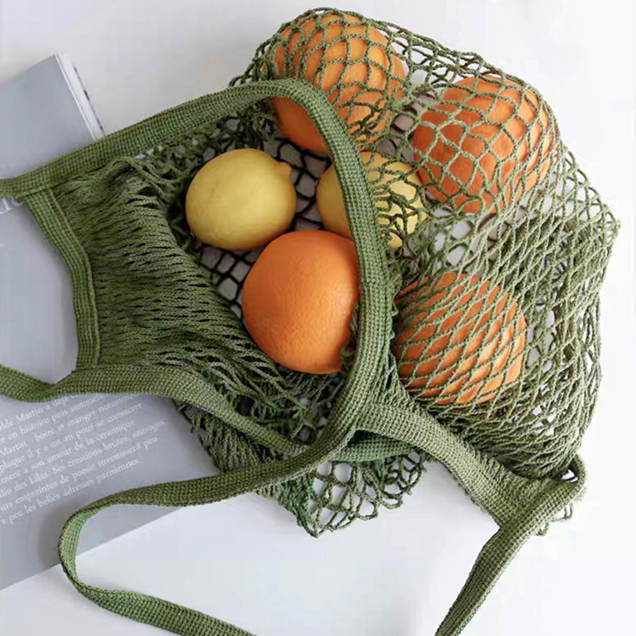 Close-up of Green cotton net shopper bag filled with oranges and lemons, ideal for errands and gifting.