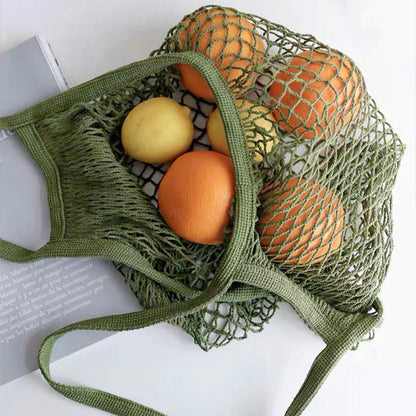 Close-up of Green cotton net shopper bag filled with oranges and lemons, ideal for errands and gifting.