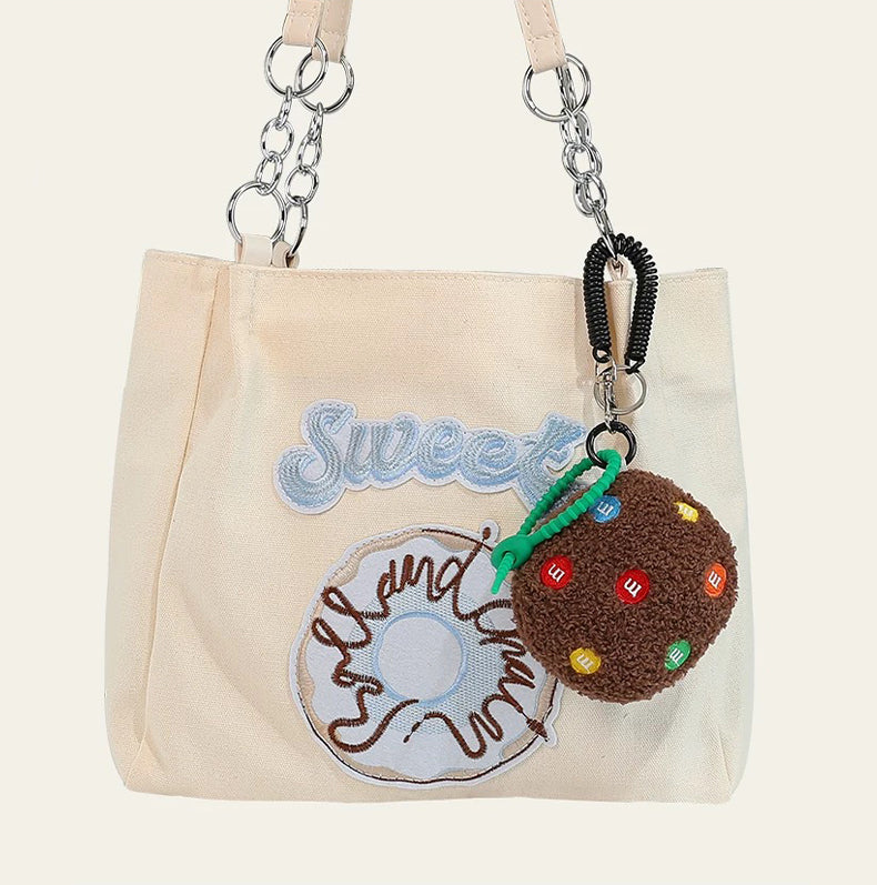 Dark brown Cookie Bag Charm hanging on a tote bag, easy to attach to bags and phones.