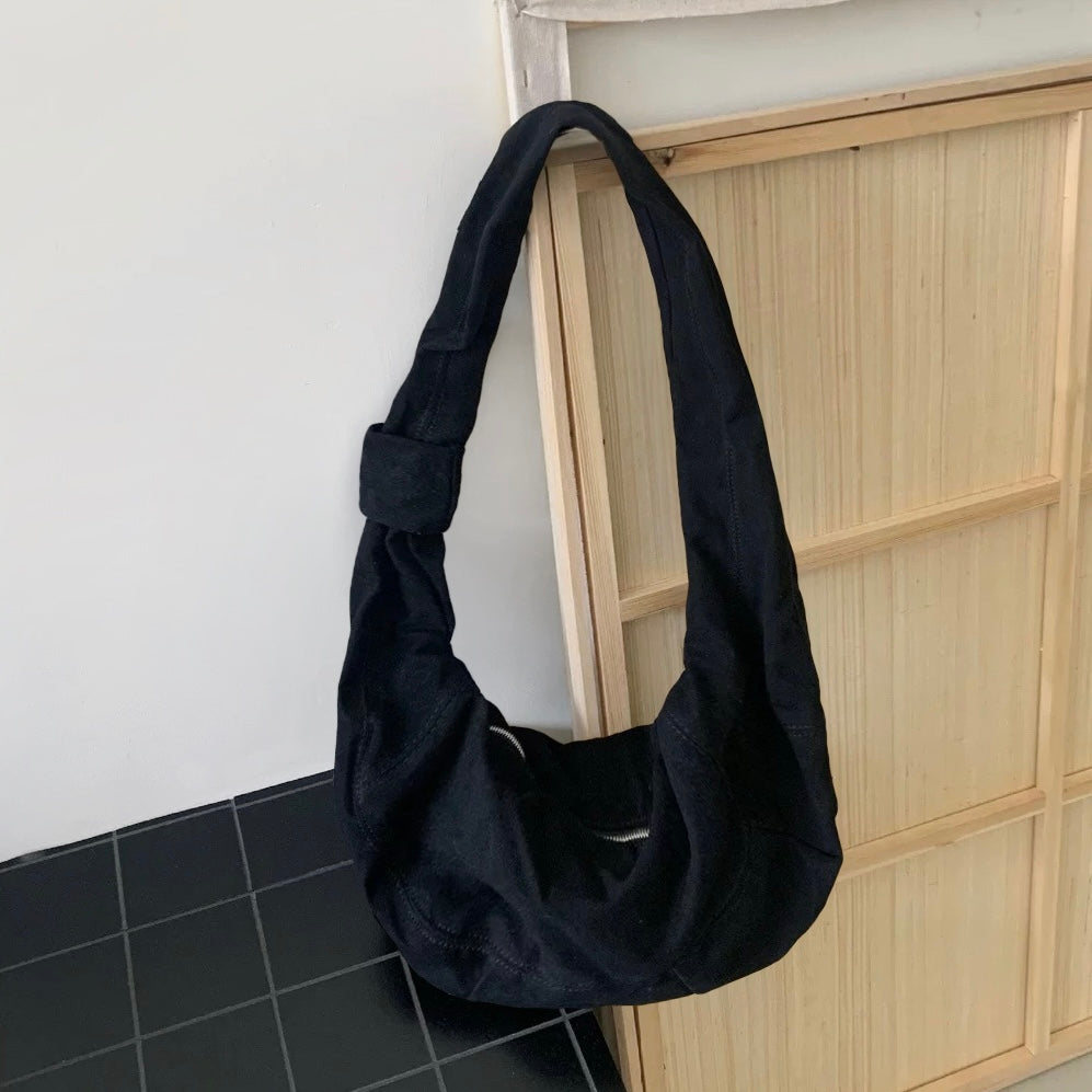 Classic black corduroy crescent bag hanging in a minimalist studio setting.