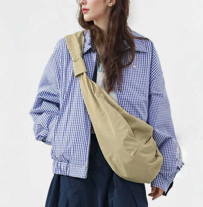 Model wearing a large khaki corduroy crescent bag over a checkered jacket.