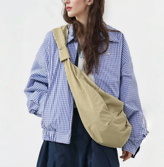 Model wearing a large khaki corduroy crescent bag over a checkered jacket.