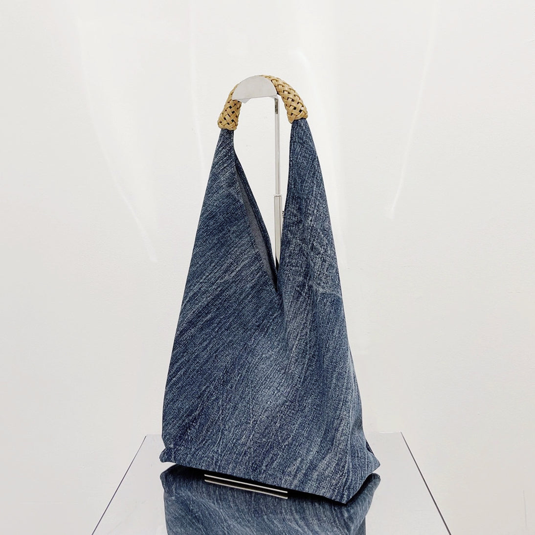 Front view of Denim shoulder bag with a unique triangular shape and braided straw-look handles.