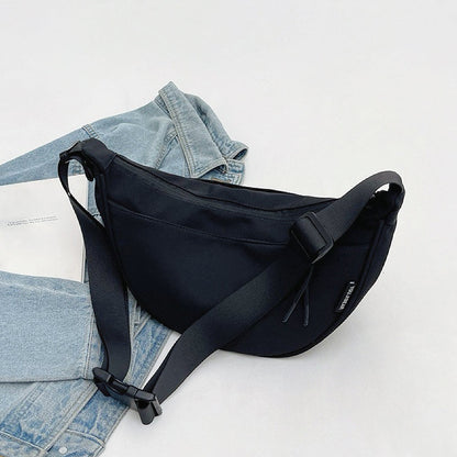 Black nylon crescent crossbody bag lying flat with denim; durable material ideal for casual outfit.
