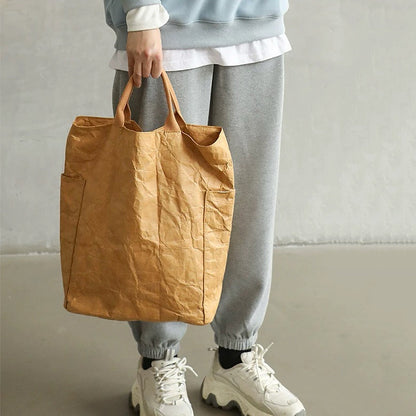 A person holding a tan kraft-paper-textured tote bag, showcasing a modern industrial fashion look.