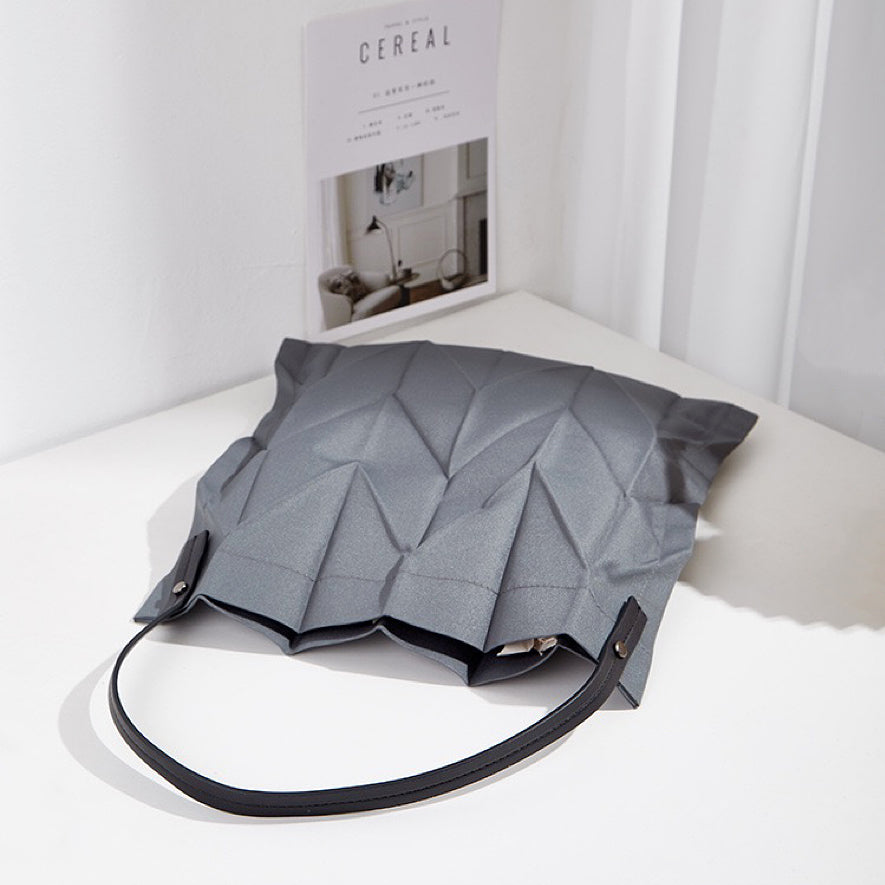 Grey pleated shopper bag resting on a table; modern minimalist aesthetic suited for office and daily commutes.