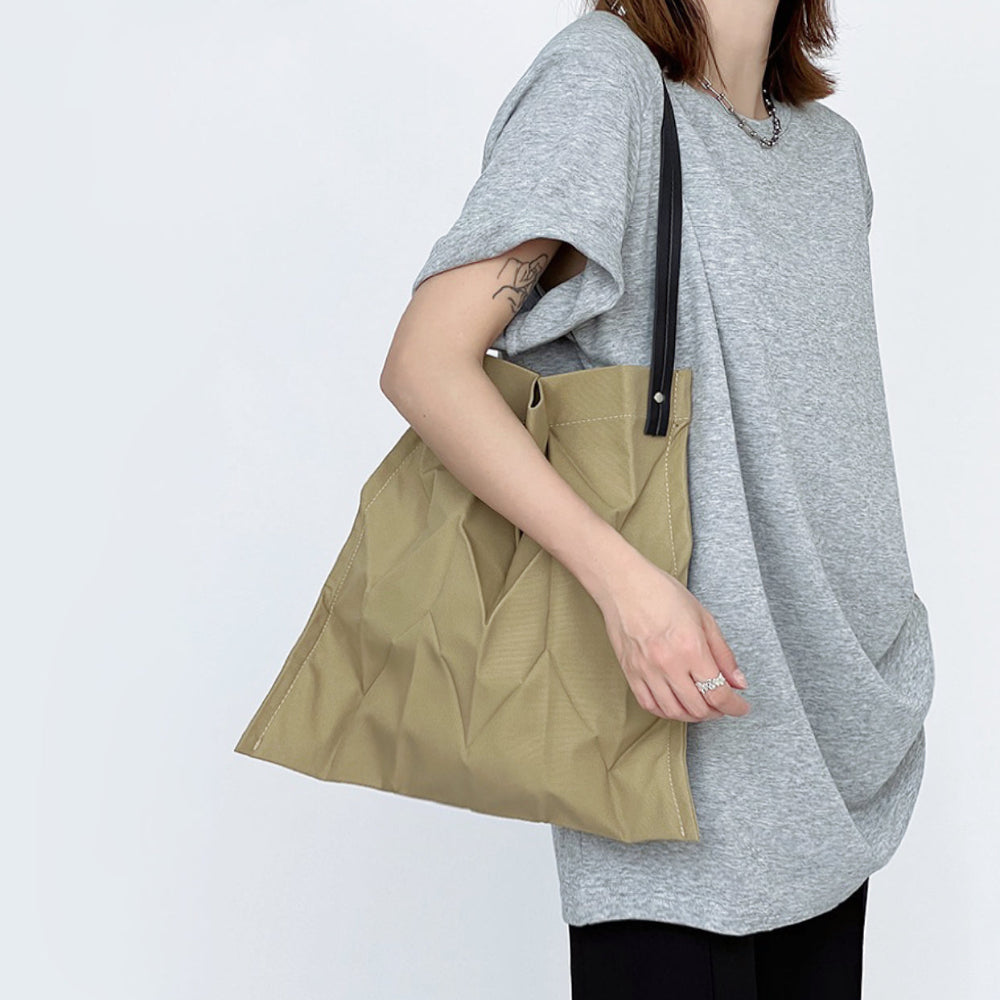 Model wearing khaki pleated bag on shoulder; lightweight fabric perfect for long city walks and sightseeing.