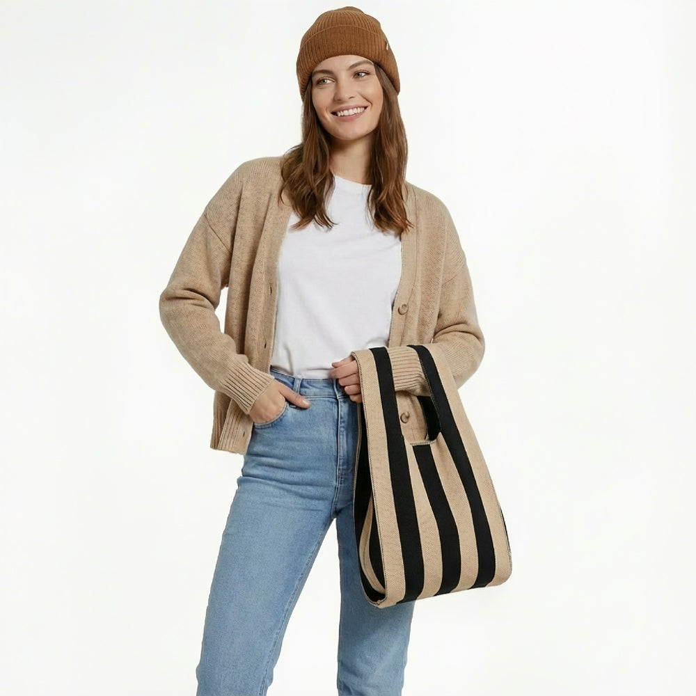 A woman wearing a brown cardigan and jeans holding a black and khaki stripe woven tote bag, showcasing French-chic style.