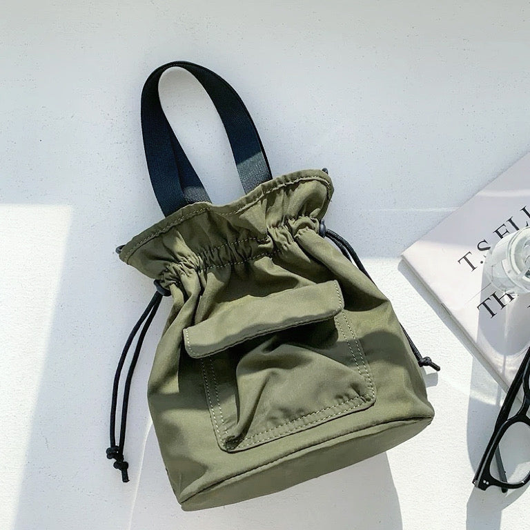 Olive green mini nylon bucket bag with a functional front utility pocket.