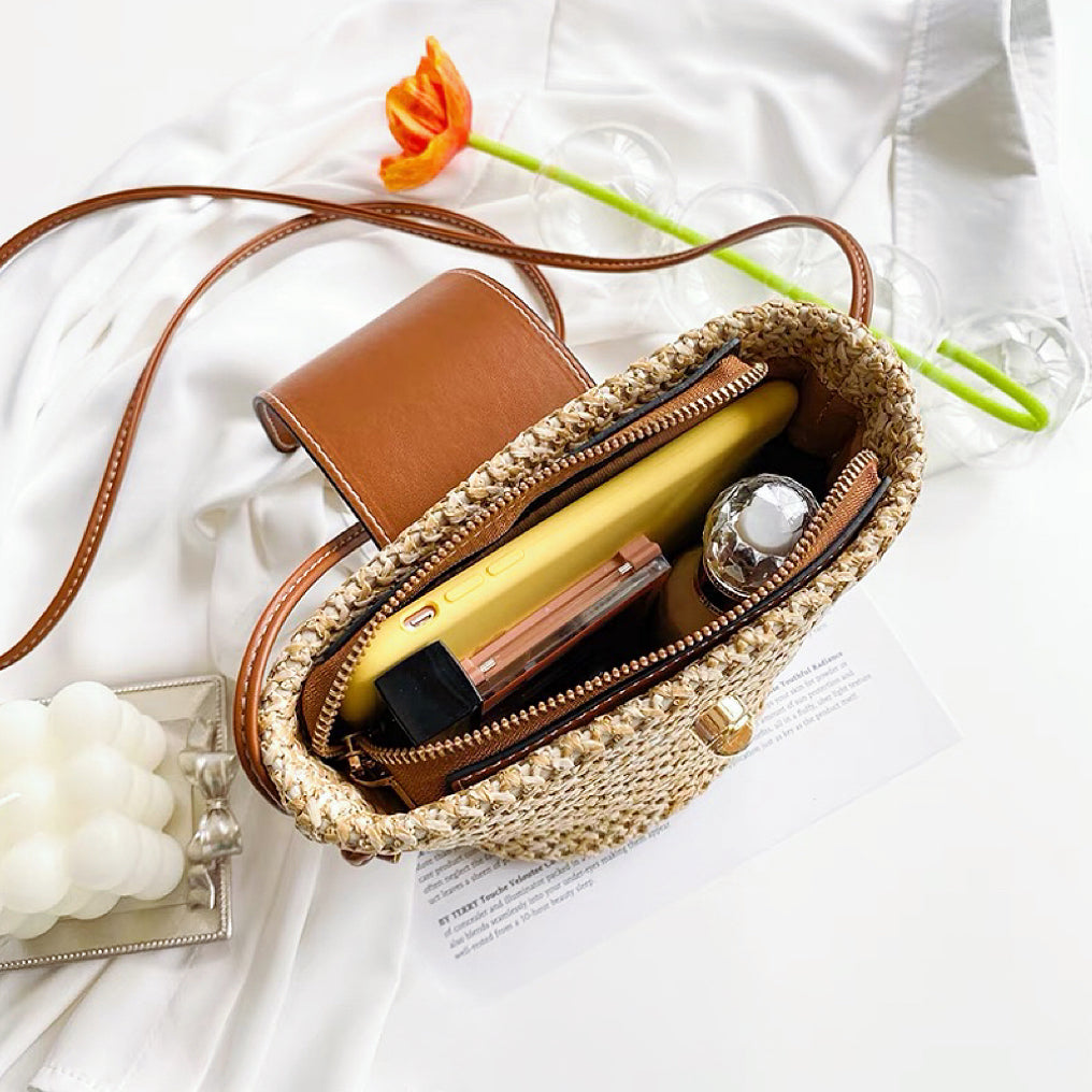 Angled view of Open mini raffia straw  bucket crossbody bag with phone and cosmetics inside