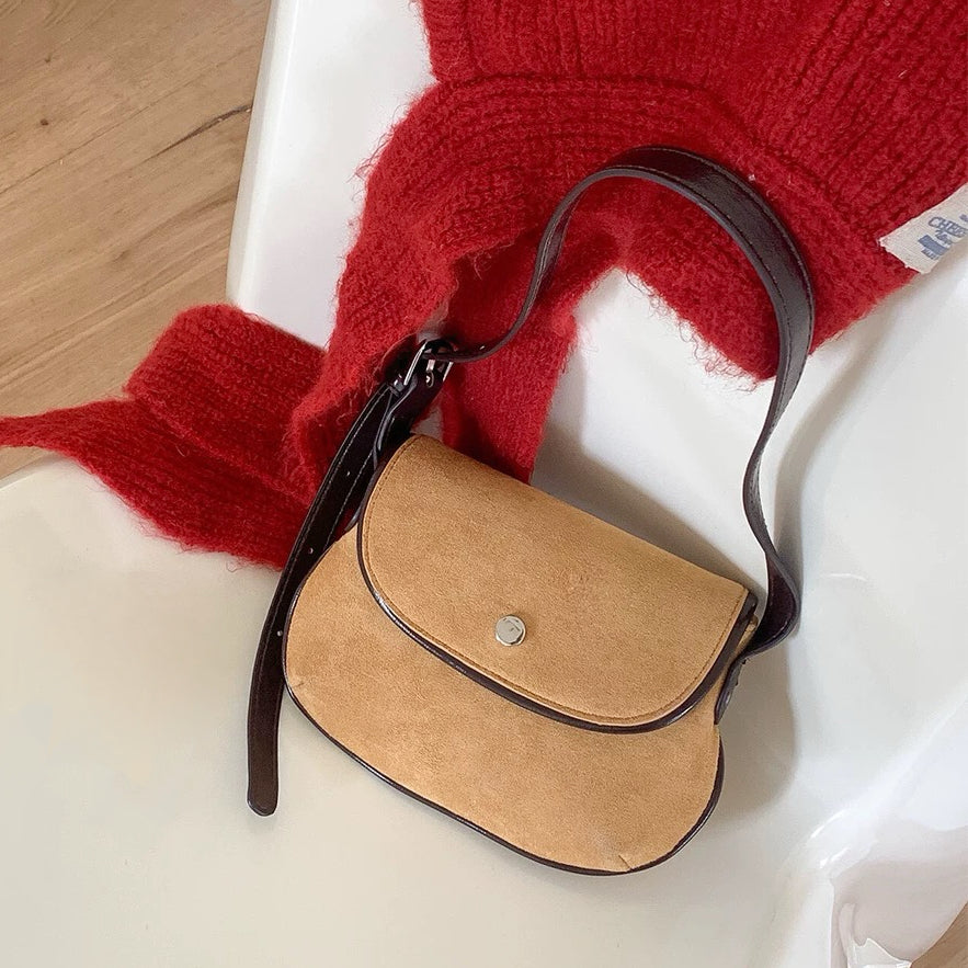 Front view of the khaki mini suede saddle bag on a clean background beside a red sweater.