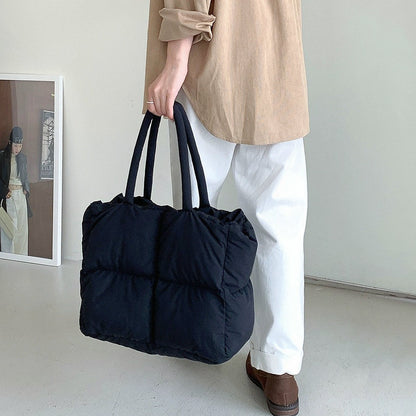 Person holding a black padded nylon tote bag with two top handles.