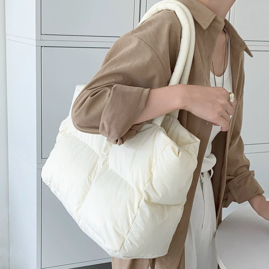 Model wearing the cream white padded tote bag on her shoulder over a brown shirt.