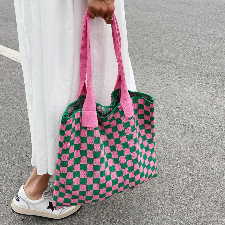 Handheld view of the pink and green checkered knit bag, showcasing its flexible casual shape.