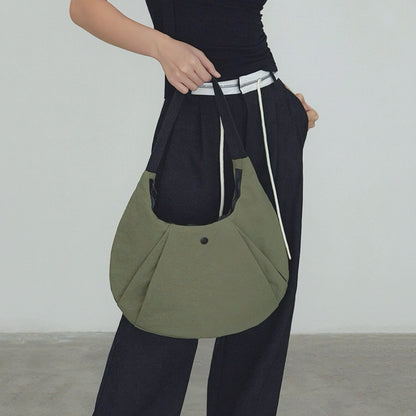 Model carrying an olive green nylon  crescent bag handheld , ideal for city walks and gifting.