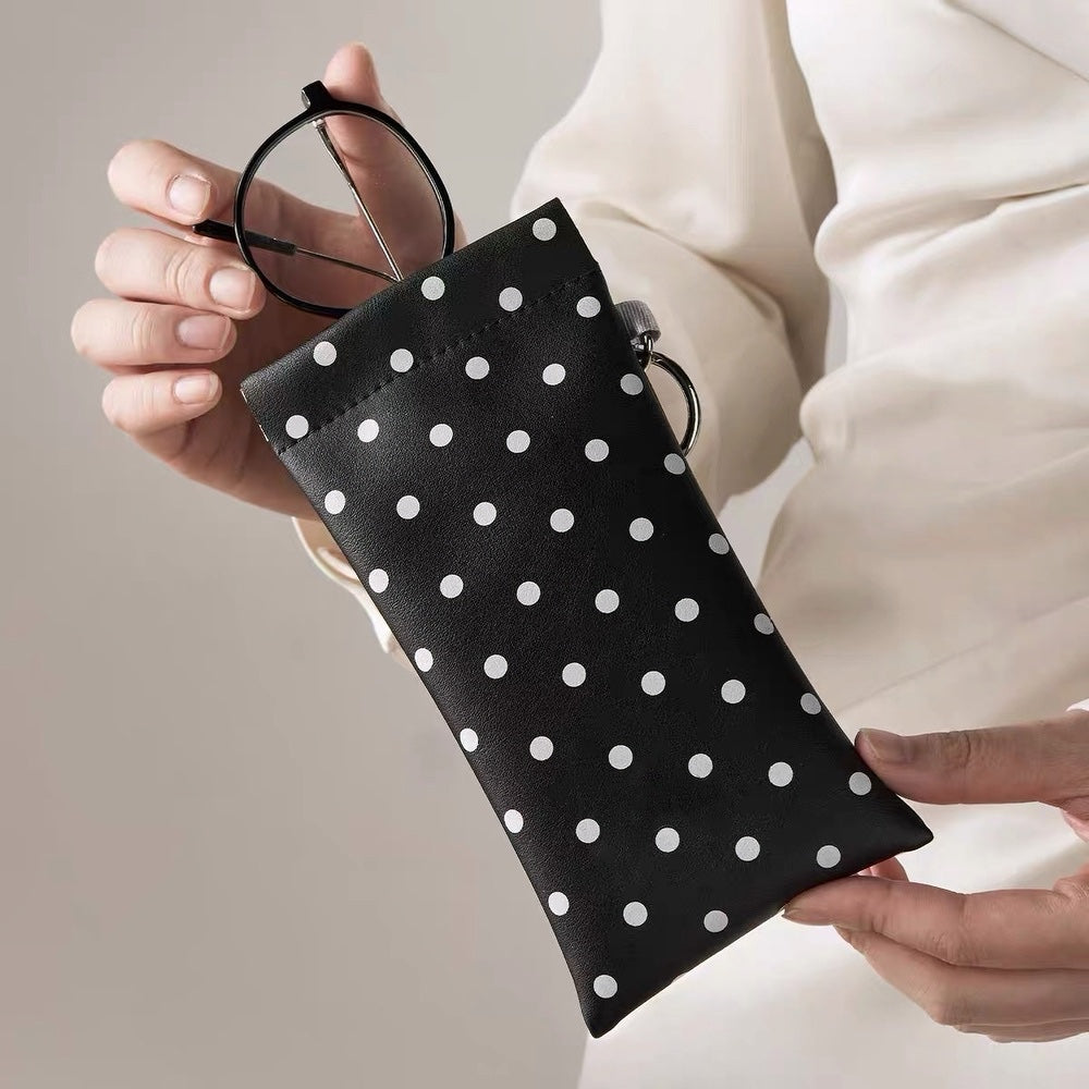 Close-up view of hands holding the black polka dot PU leather glasses pouch with metal spring ring.