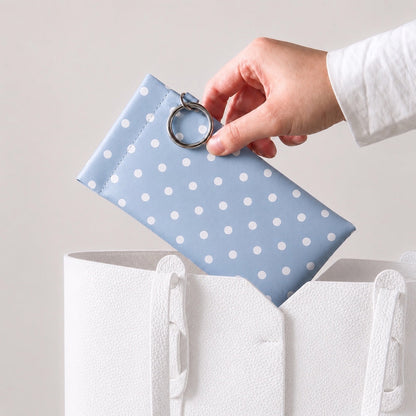 A light blue polka dot glasses pouch being placed into a white tote bag for everyday commuting.