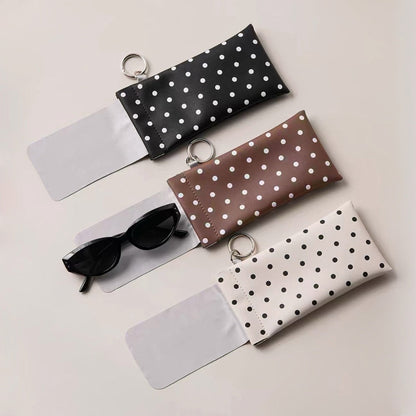 Flat lay of black, brown, and cream white polka dot glasses cases showing attached microfiber lens cloths and metal rings.