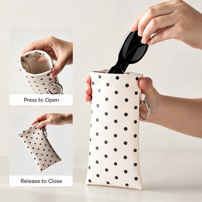 Demonstration of squeezing the metal spring sides to open and close the cream polka dot sunglasses case.