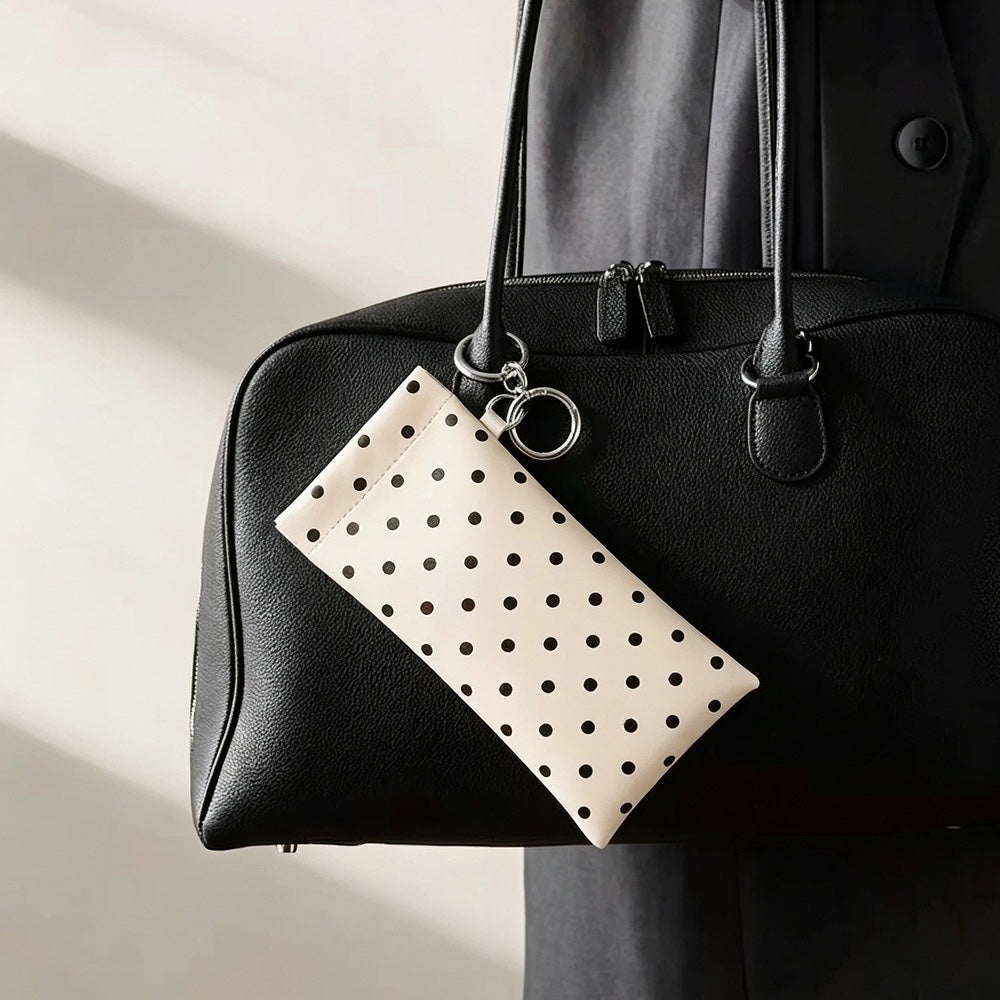 Cream white polka dot glasses clipped onto the exterior handle of a black leather handbag using its metal ring.