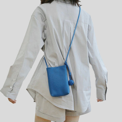 Model carrying a blue Polycolor hanging ball leather bag as crossbody, clean minimalist look.