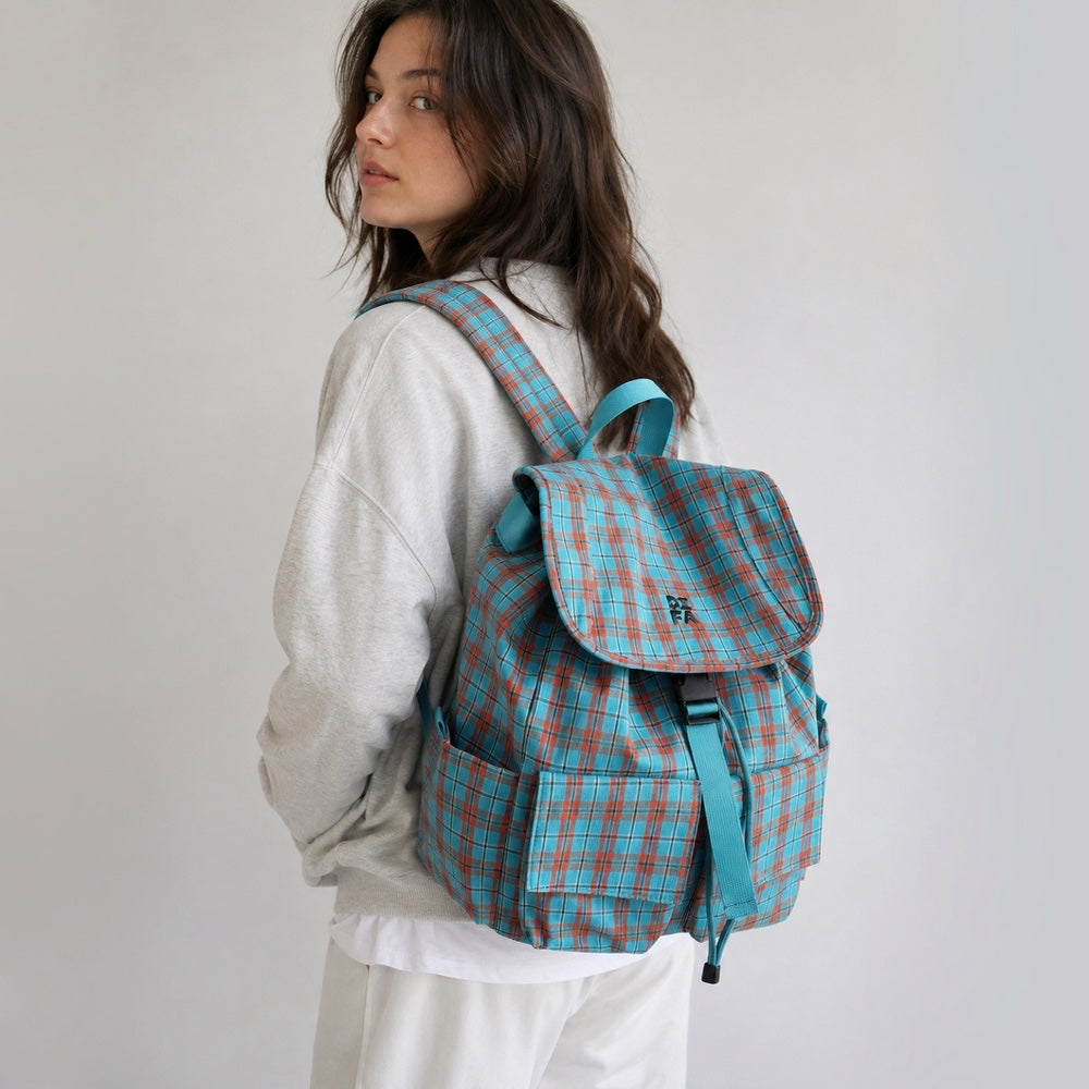 Side profile view of a model in a white sweatshirt carrying the blue plaid nylon laptop backpack.