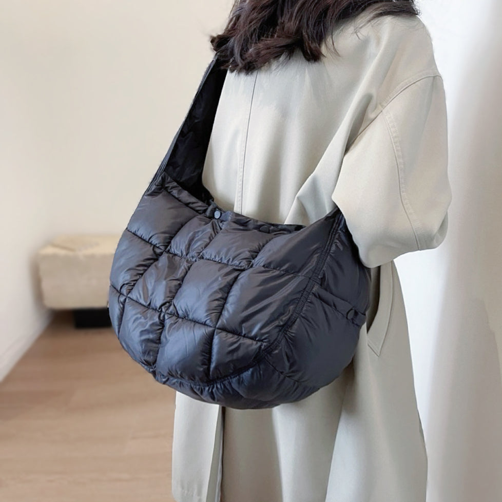 Model carring a black puffy crossbody bag as crossbody; minimalist and functional quilted bag for urban chic.