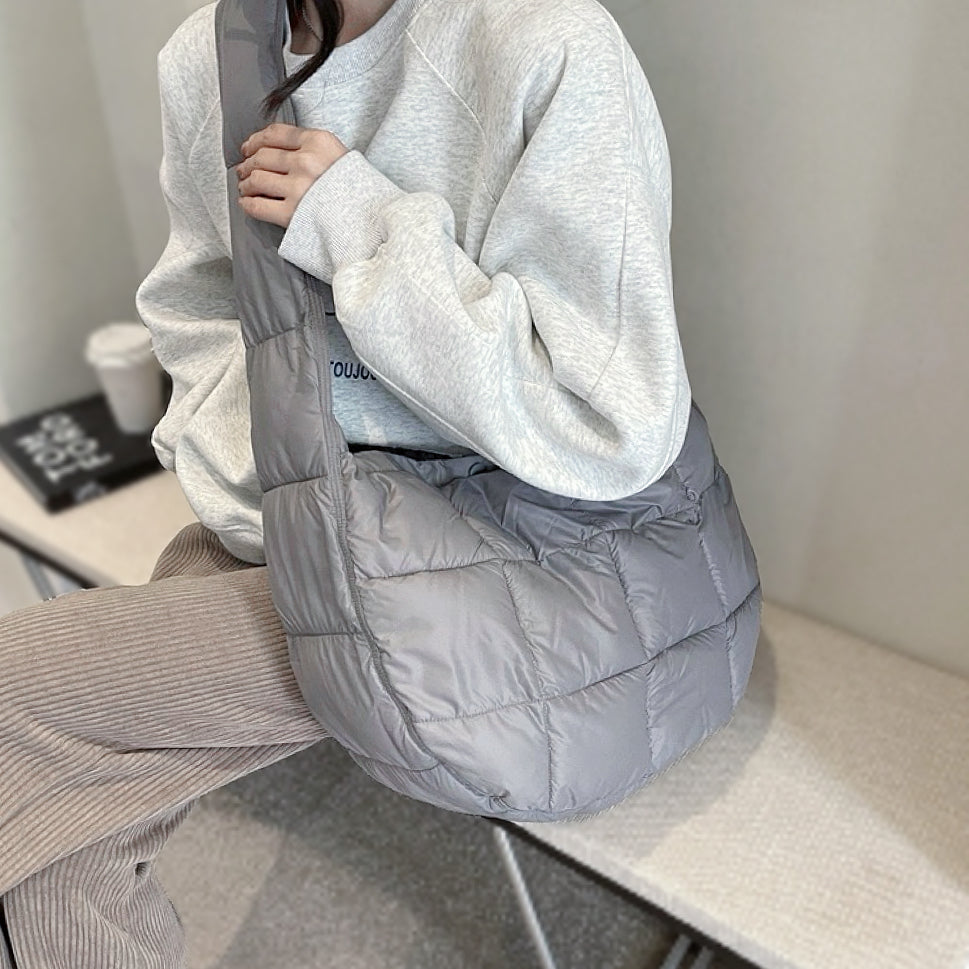 Side view of a grey quilted semicircle bag worn by model, showing the wide shoulder strap. 