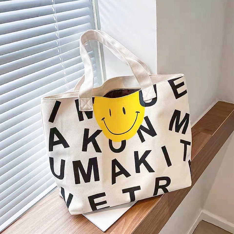 Close-up of canvas tote bag with black letters and a yellow smile face, ideal for errands and gifting.