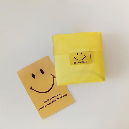 Foldable yellow oxford cloth shopper bag with a smiley face tag, beside a matching Smile to life card.