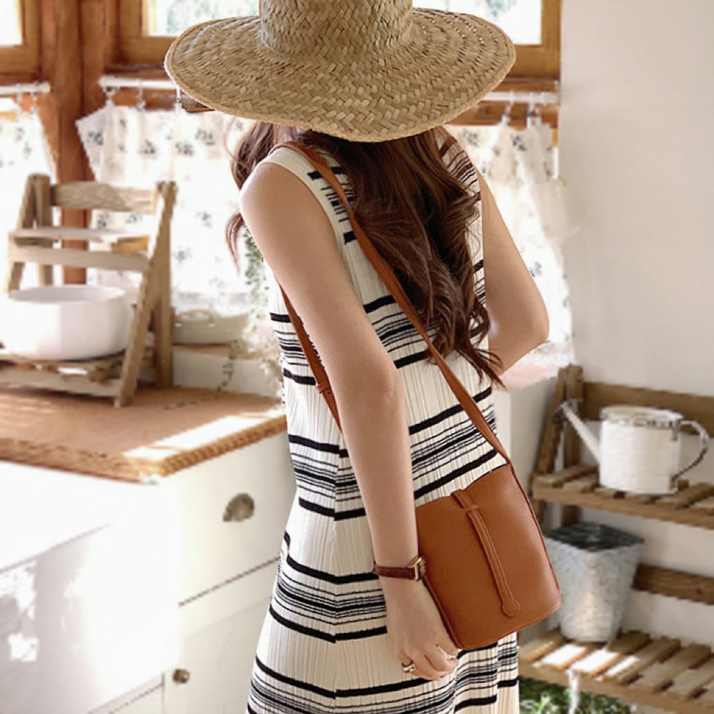 Side profile showing the structured shape of the brown lychee leather crossbody bag worn by model.