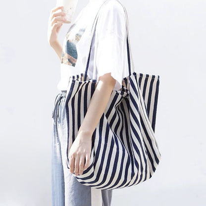 Model styling navy blue striped tote over shoulder, durable canvas fabric ideal for students and campus life.