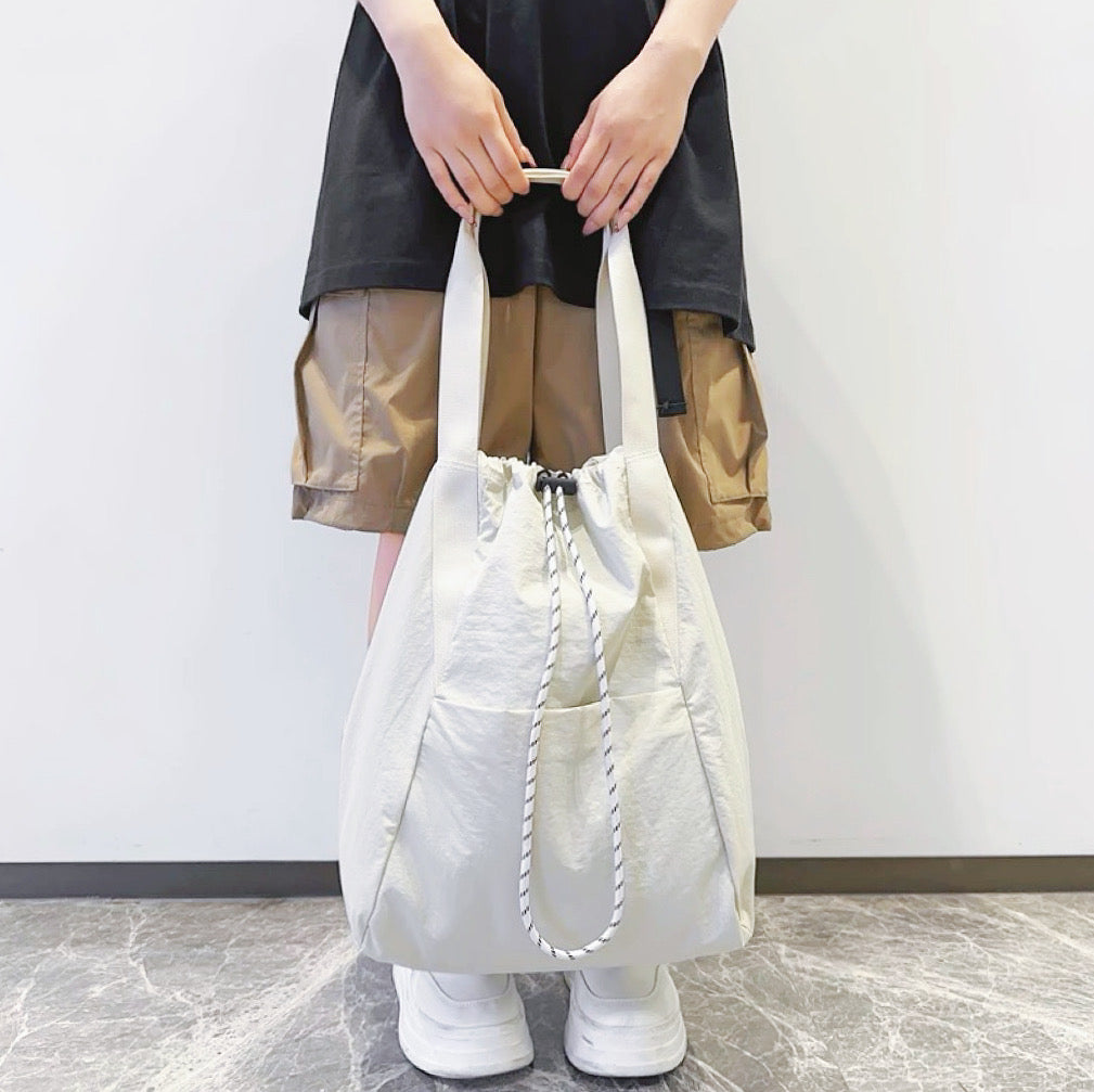 A model holding the white bag as a tote in front, showing the outer zip pocket for quick-access storage.