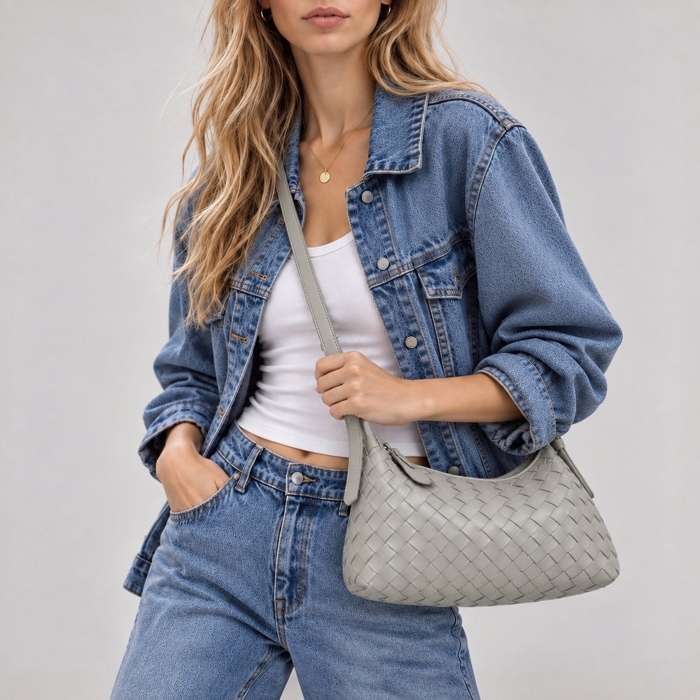 Model styling a light grey woven crossbody bag with a blue denim jacket.