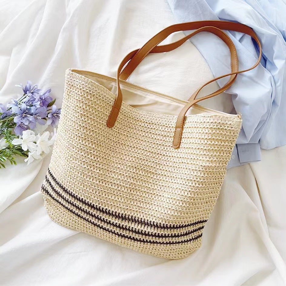 Front view of Beige woven straw tote bag with brown PU leather straps and three black stripes.