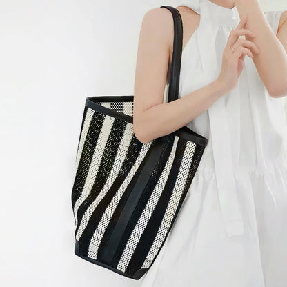 Model wearing the large black and white striped raffia bucket bag as shoulder bag.