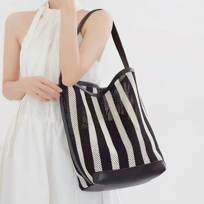Model holding the large woven striped raffia bucket bag as chic style.