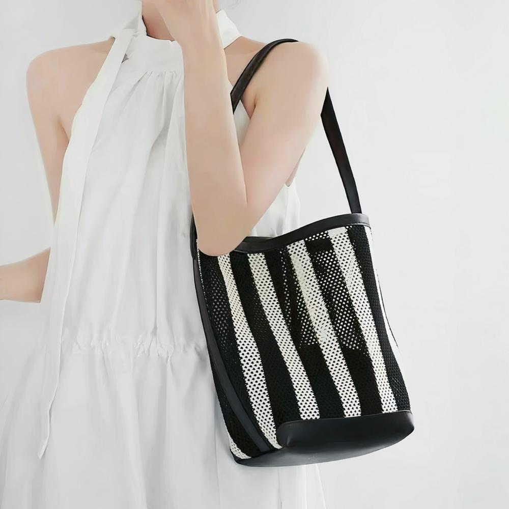Model carrying the small black and white striped raffia bucket bag as shoulder bag.